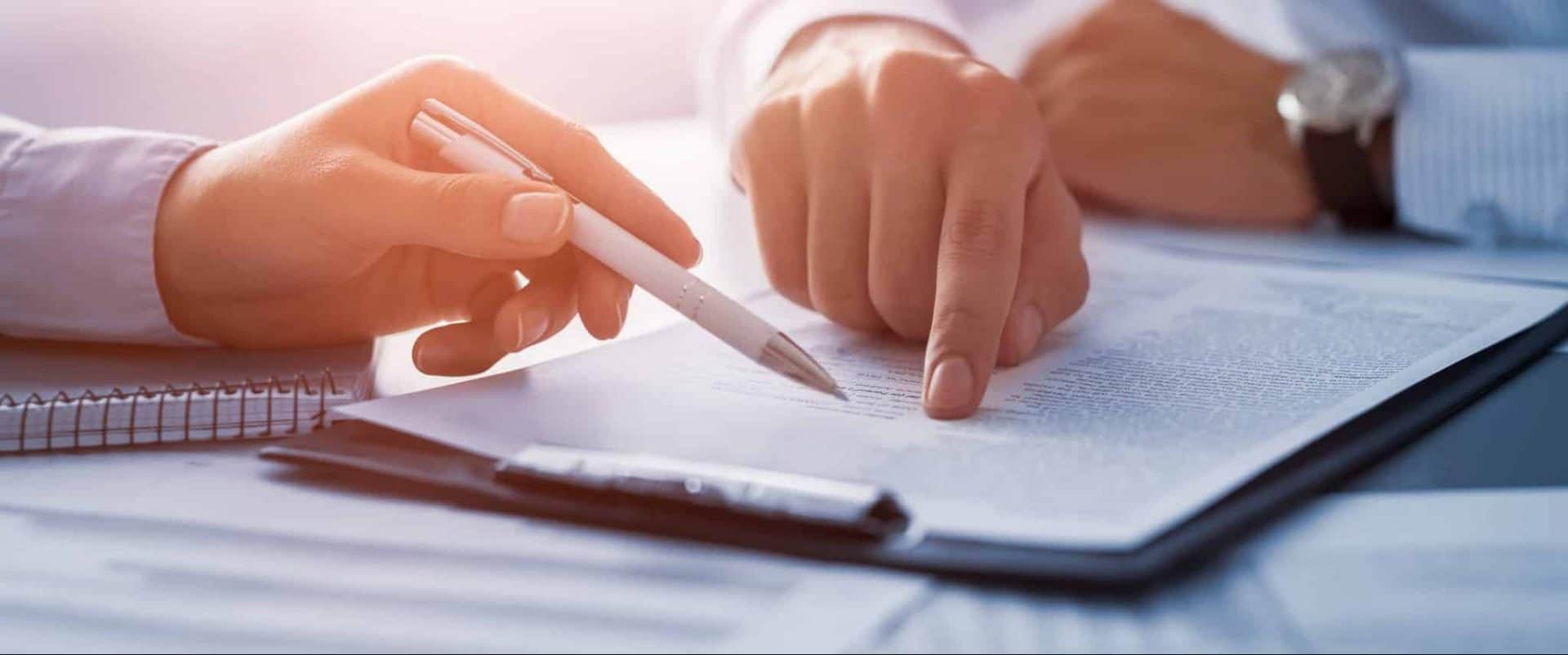 Nærbillede af to personer, der kigger på et dokument og peger på indholdet med pen og finger.